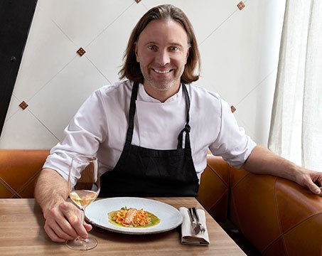 A chef presenting a gourmet seafood dish with a glass of white wine in an elegant dining setting | MSC Cruises A chef presenting a gourmet seafood dish with a glass of white wine in an elegant dining setting | MSC Cruises